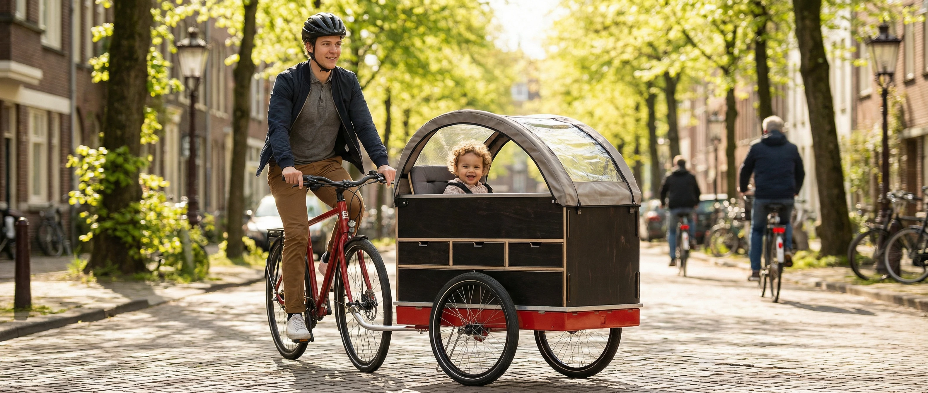 Parent cycling with child in a modular cargo bike trailer through a tree-lined bike lane